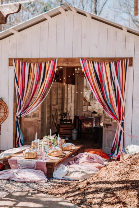 An outdoor dining table surrounded by cushions and streamers
