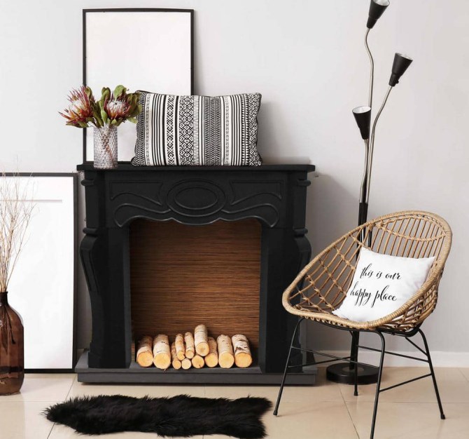 A living room with a faux black ornate mantelpiece backed with wallpaper and filled with logs