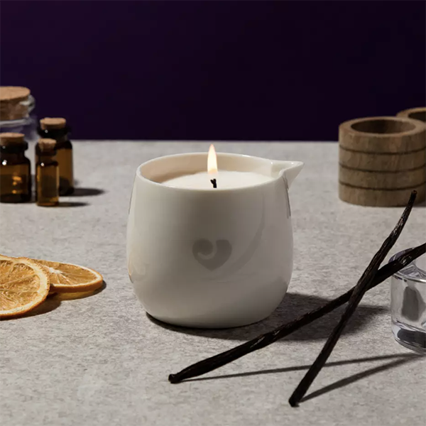 A massage candle surrounded by essential oils, fruit slices, and other aromatic items