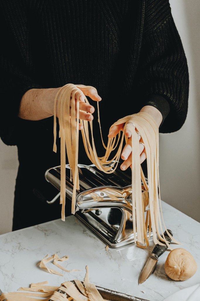 A person holding handmade pasta in front of a pasta maker