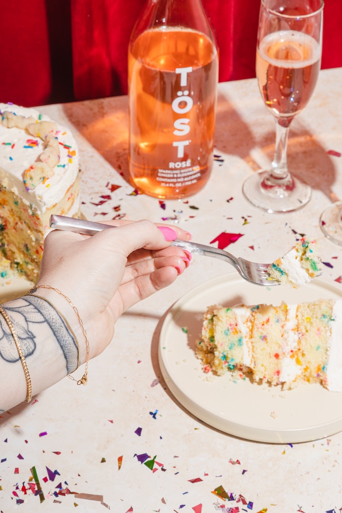 A slice of funfetti cake surrounded by rainbow confetti and rose wine