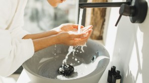 Spa treatment. Bathroom with white walls full of sun light. Black metal furniture. Grey stone sink. Person in bathrobe. Trendy interior design