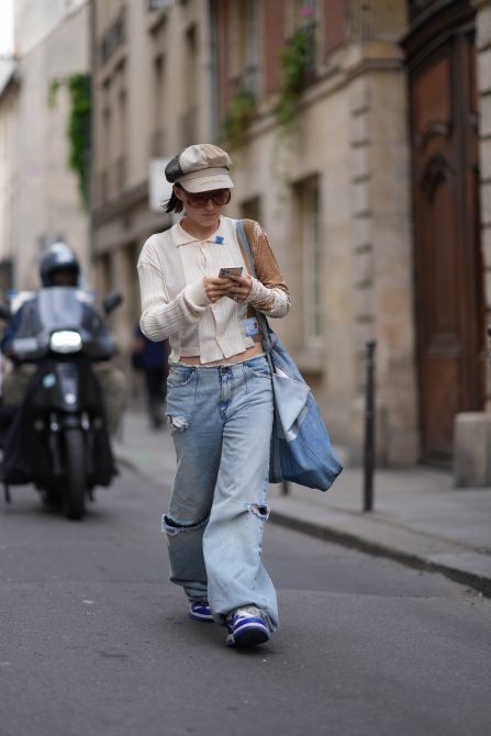 A guest wears a paperboy hat, a brown and white ribbed shirt, blue ripped denim flared jeans, blue sneakers, outside Cecilie Bahnsen, during the Womenswear Spring/Summer 2024 as part of Paris Fashion Week on September 27, 2023 in Paris, France.