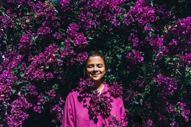 Beautiful happy woman in a bright shirt against the background of a bright purple bougainvillea.