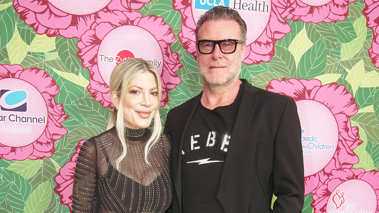 Tori Spelling, a white woman with blonde hair and wearing a black sheer dress with Dean McDermott, a white man with brown hair and glasses and wearing a blazer and shirt.