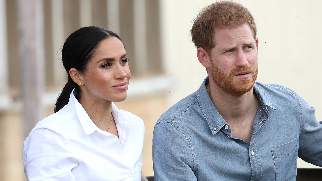 Meghan Markle, a biracial woman wearing a white shirt and Prince Harry a white man with ginger hair wearing a denim button down.