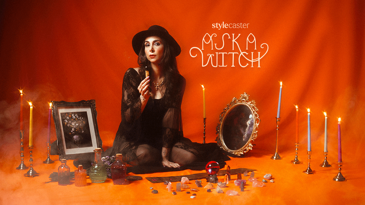 A witch woman holding palo santo, sitting on the floor, surrounded by Tarot cards, crystals, and lit candles, ready to tell you all about your future.