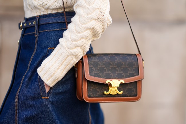 A street style star wearing a white sweater, jeans, and a Celine Triomphe crossbody bag at Paris Fashion Week