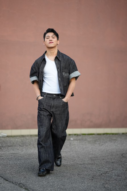 A man wears a black Gucci denim opened jacket with cuffed short sleeves, a white t-shirt, black denim flared pants, black leather pointed shoes