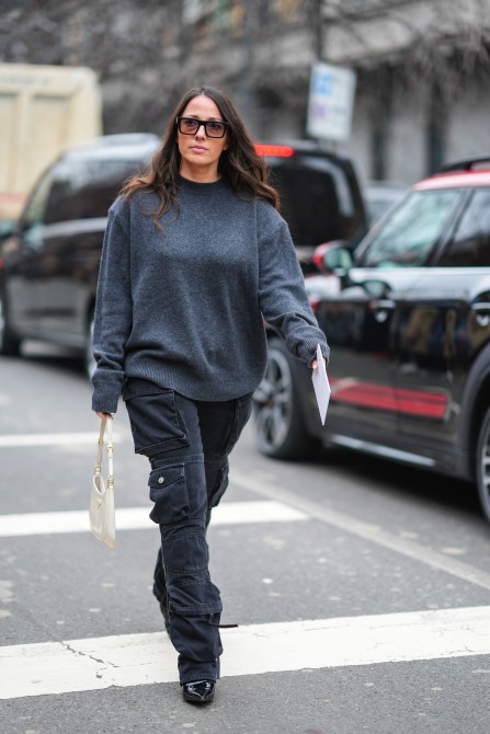 A guest wears a gray oversized sweater, cargo pants, a white leather bag, and black leather pointed shoes during the Milan Fashion Week on February 22, 2024 in Milan, Italy.