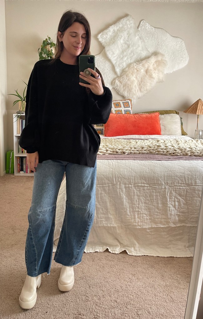 A woman wearing a black oversized sweater with blue denim barrel jeans and cream clogs