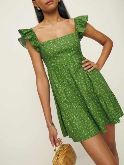 A woman wearing a green floral print dress with ruffled sleeves.