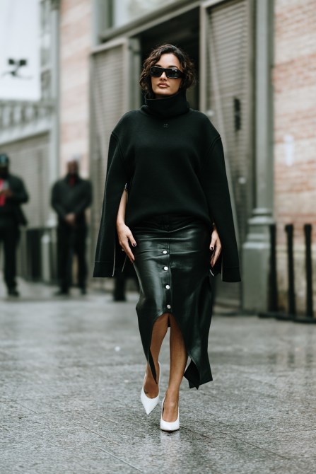 a curve model wears a black turtleneck sweater and leather skirt with white pumps