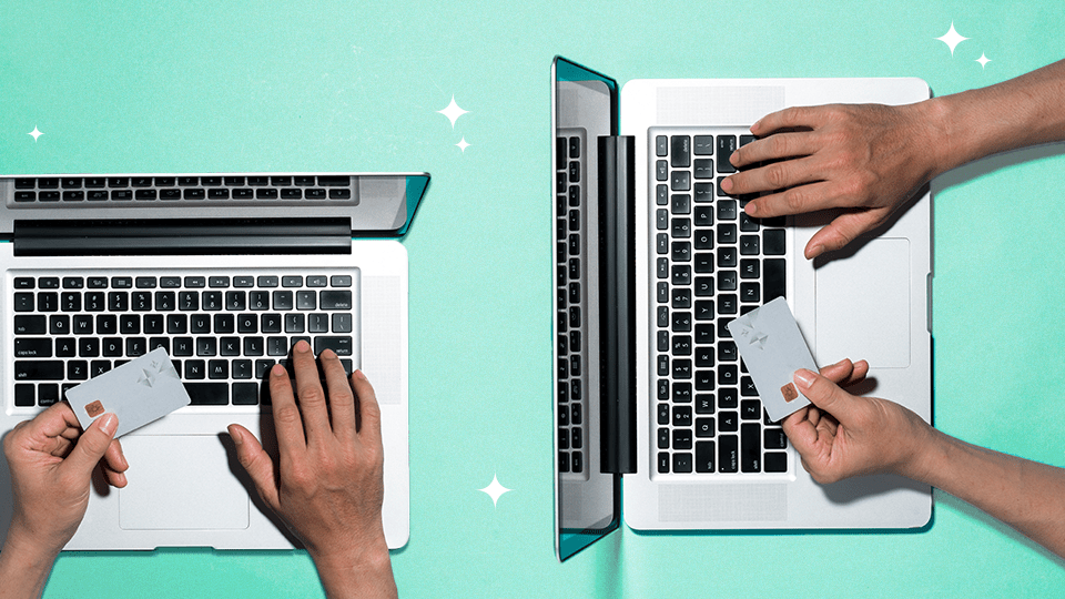 An overhead view of two laptops with hands typing and holding credit cards.
