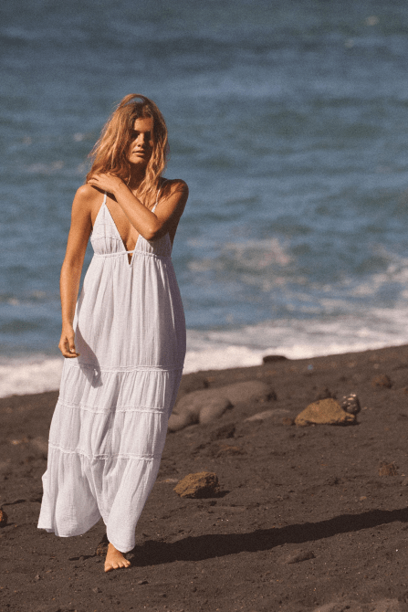 A model walking on the beach in the Zara Embroidered Midi Dress in white