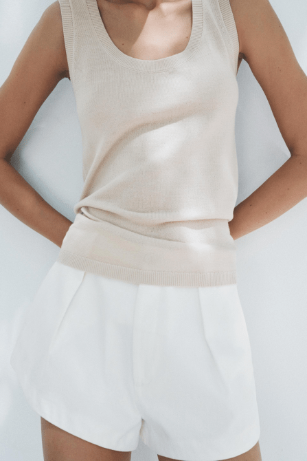 A model wearing the Zara Plain Knit Wool Top in beige with white pleated shorts.