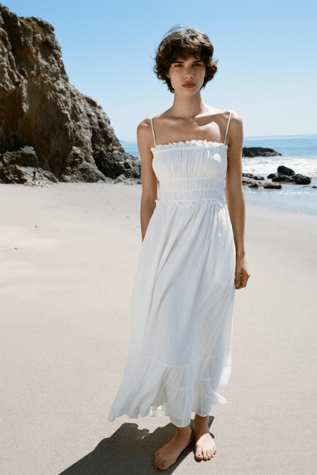 A model wearing the Zara Voluminous Gauze Midi Dress in white while standing on a beach