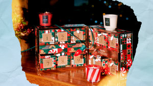 A ifestyle shot of Voluspa's 2025 advent calendar on a wooden table with Christmas lights wrapped around it